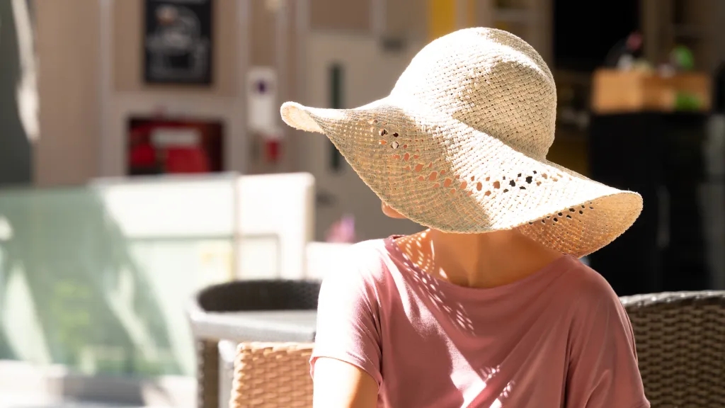 Frau im Café blickt in die Sonne und Hut verdeckt ihr Gesicht